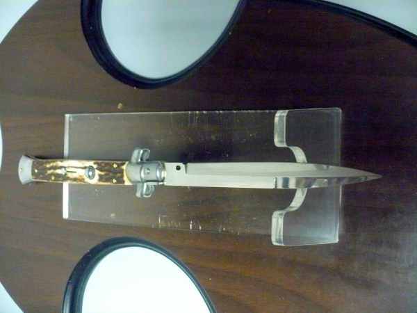 Coltello a scatto with a polished bayonet blade and mottled deer horn handle with metal fittings